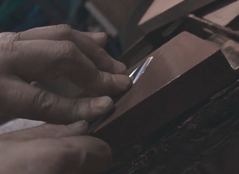 Artesano profesional amolando manualmente a tijeras profesionales de peluquería hecha a mano.